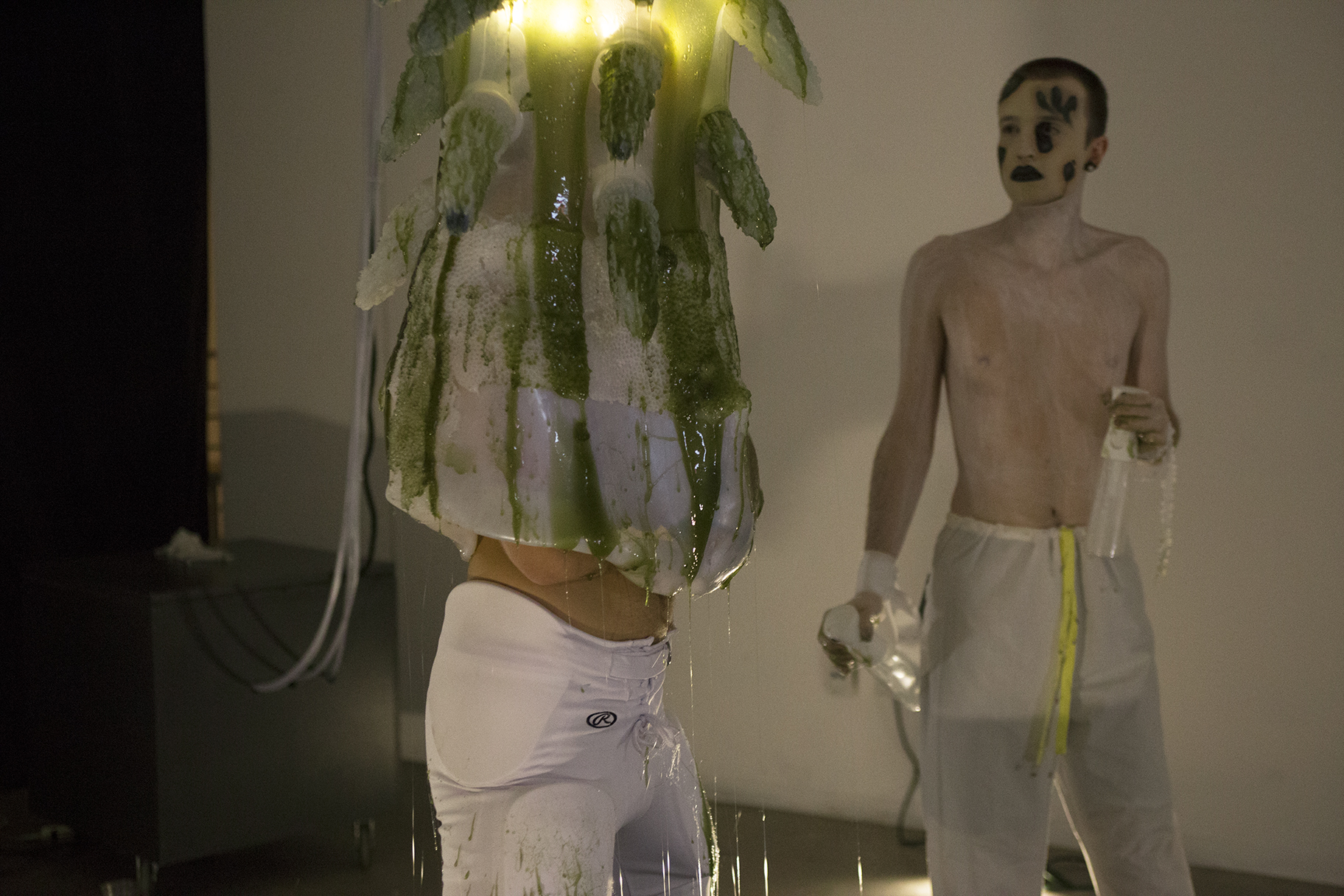 A man engulfed in a gelatenous form covered in tentacles knealing over a pool of green slime in a gallery